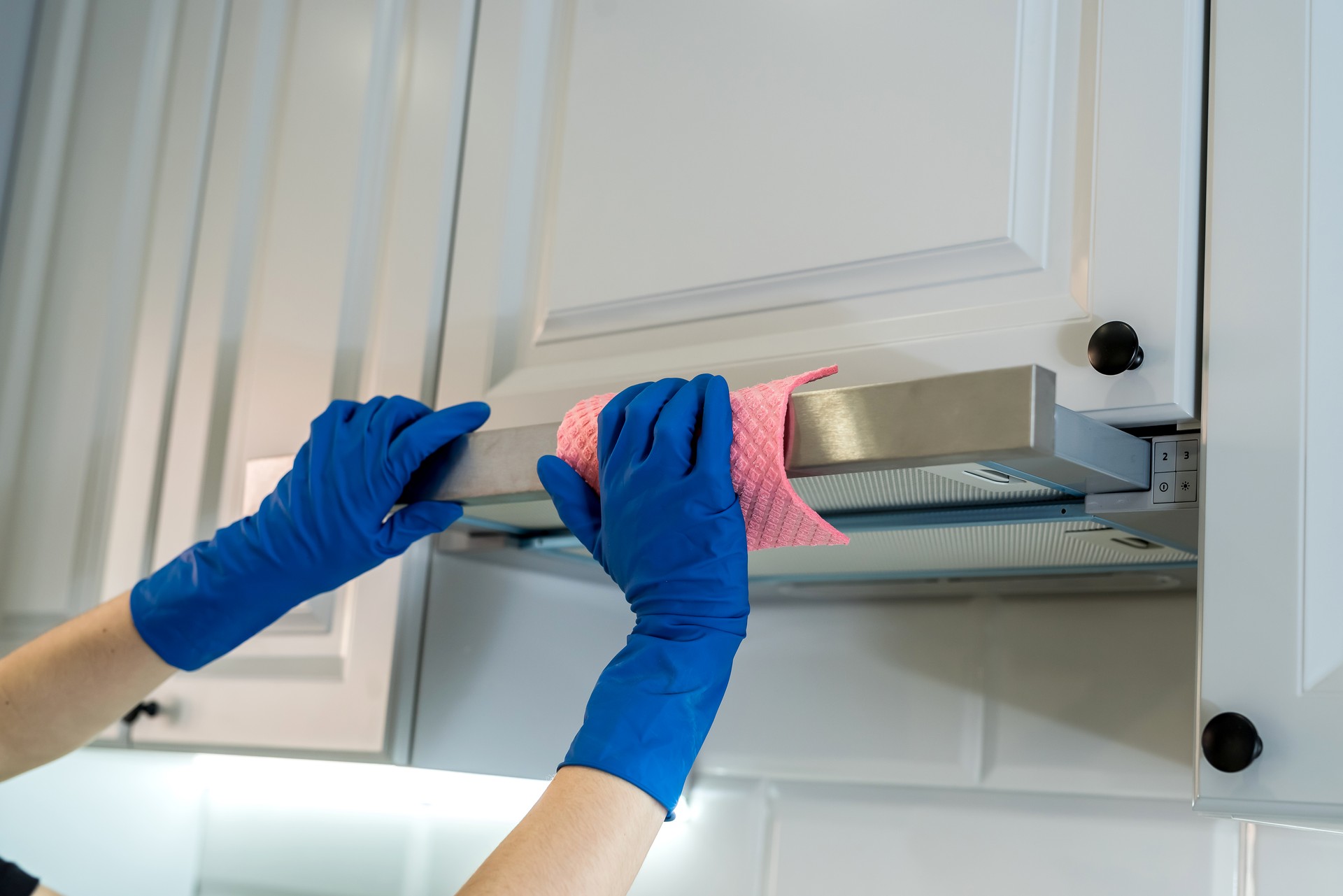 female hand in rubber protective сleaning cooker hood with rag in kitchen.